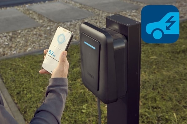 Wallbox witty plus installata su colonnina di fissaggio in esterno. In primo piano in mano lo smartphone con l’app hager charge con videata della fase di ricarica.