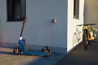 Monopattino elettrico collegato tramite cavo elettrico a una presa di ricarica witty prise montata sulla parete esterna della casa.