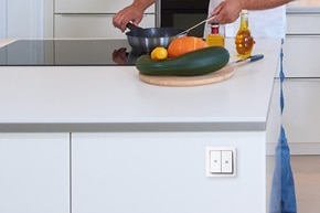 Esempio di installazione dell'interruttore per tapparelle Berker Enocean con bilanciere a 2 vie e simboli freccia per su e giù su isola della cucina. Nello sfondo un uomo sta cucinando su una piastra ad induzione