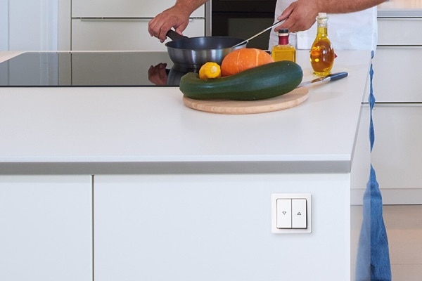 Esempio di installazione dell'interruttore per tapparelle Berker Enocean con bilanciere a 2 vie e simboli freccia per su e giù su isola della cucina. Nello sfondo un uomo sta cucinando su una piastra ad induzione