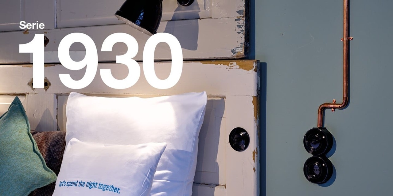 Parete di una stanza di hotel con interruttori retrò Berker neri per luce e presa con scritta Serie 1930