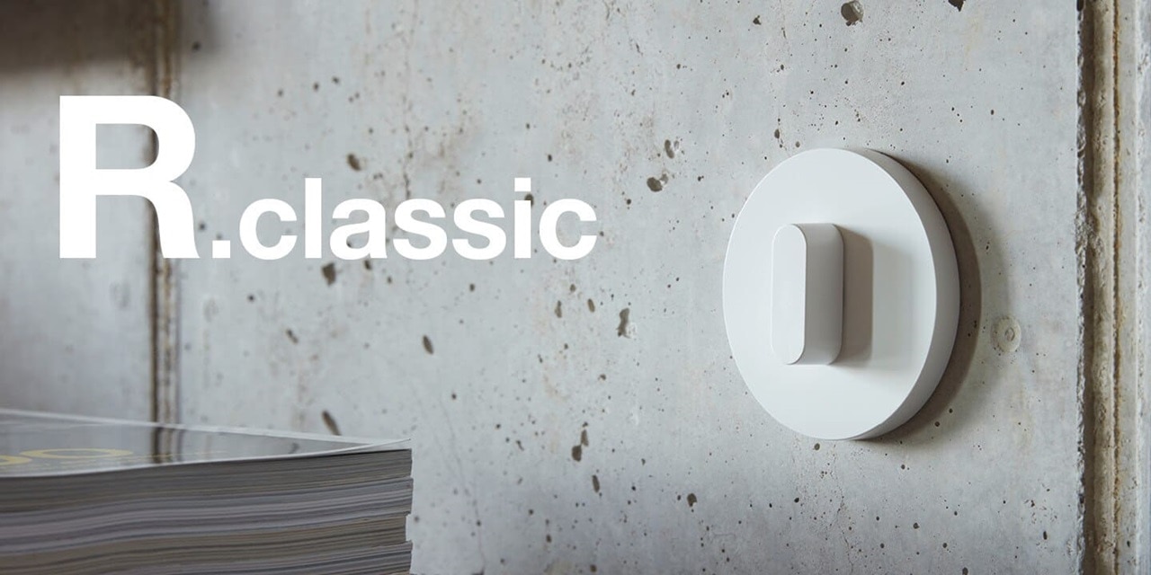 Vista del muro in cemento a vista con interruttore della luce bianco con interruttore rotativo e cornice rotonda bianca della gamma di interruttori Berker R.classic e relativa scritta