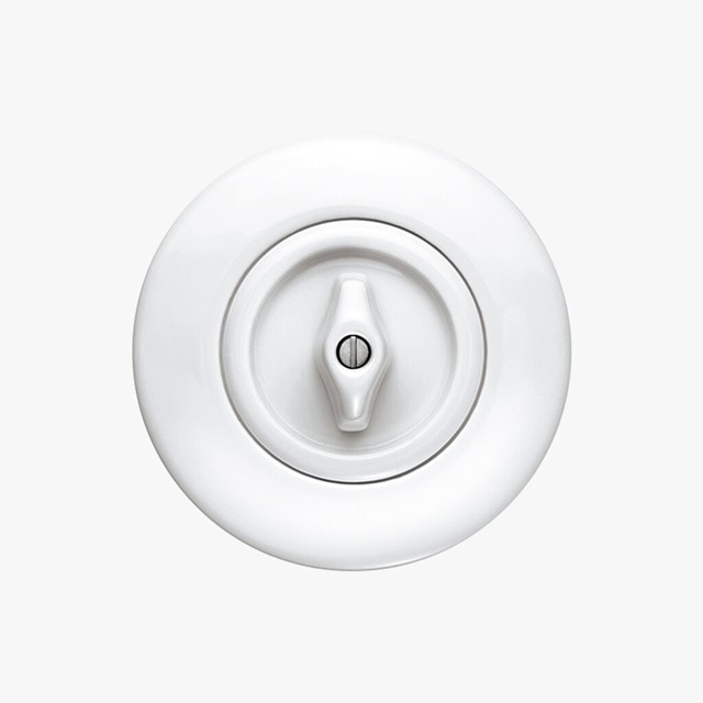 Vista frontale dell'interruttore Berker Serie 1930 con interruttore rotativo montato all’interno della cornice rotonda, entrambi in porcellana bianca su sfondo neutro grigio