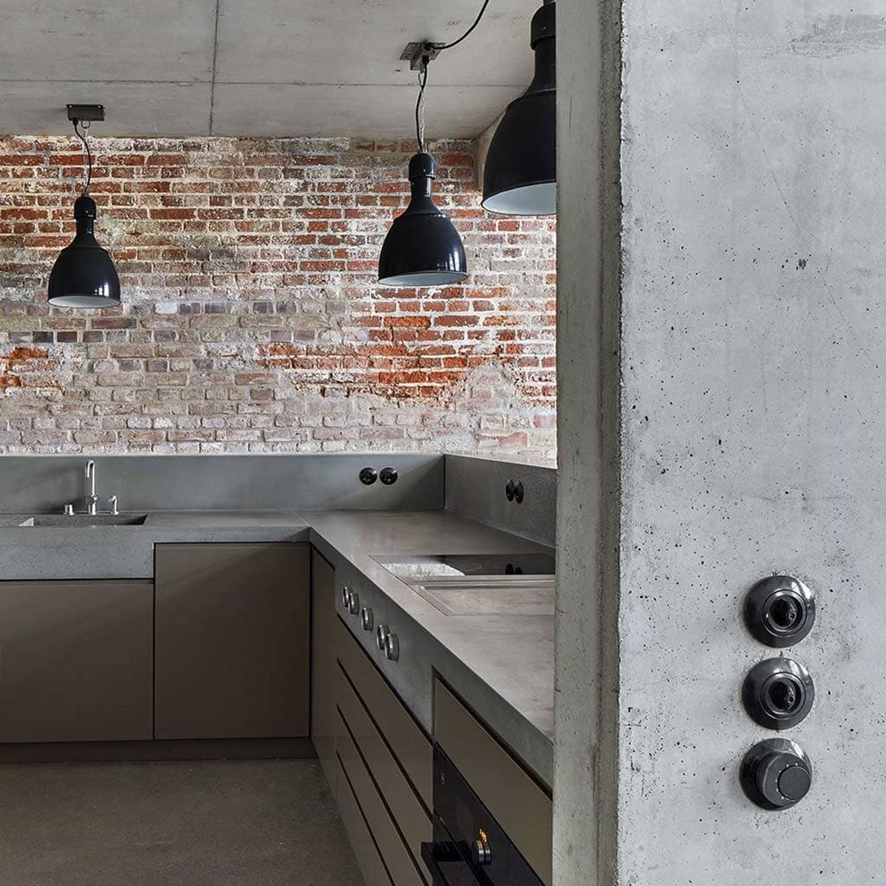 Esempio di installazione verticale di interruttori della luce Berker Serie 1930 di colore nero su parete in muratura grezza di una cucina