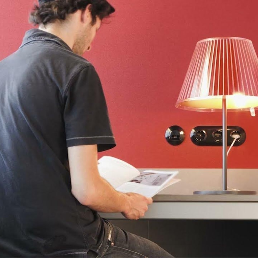 Installatore elettricista intento a leggere istruzioni di montaggio degli interruttori e prese Berker Serie 1930 di colore nero installati su parete di colore rosso arancione