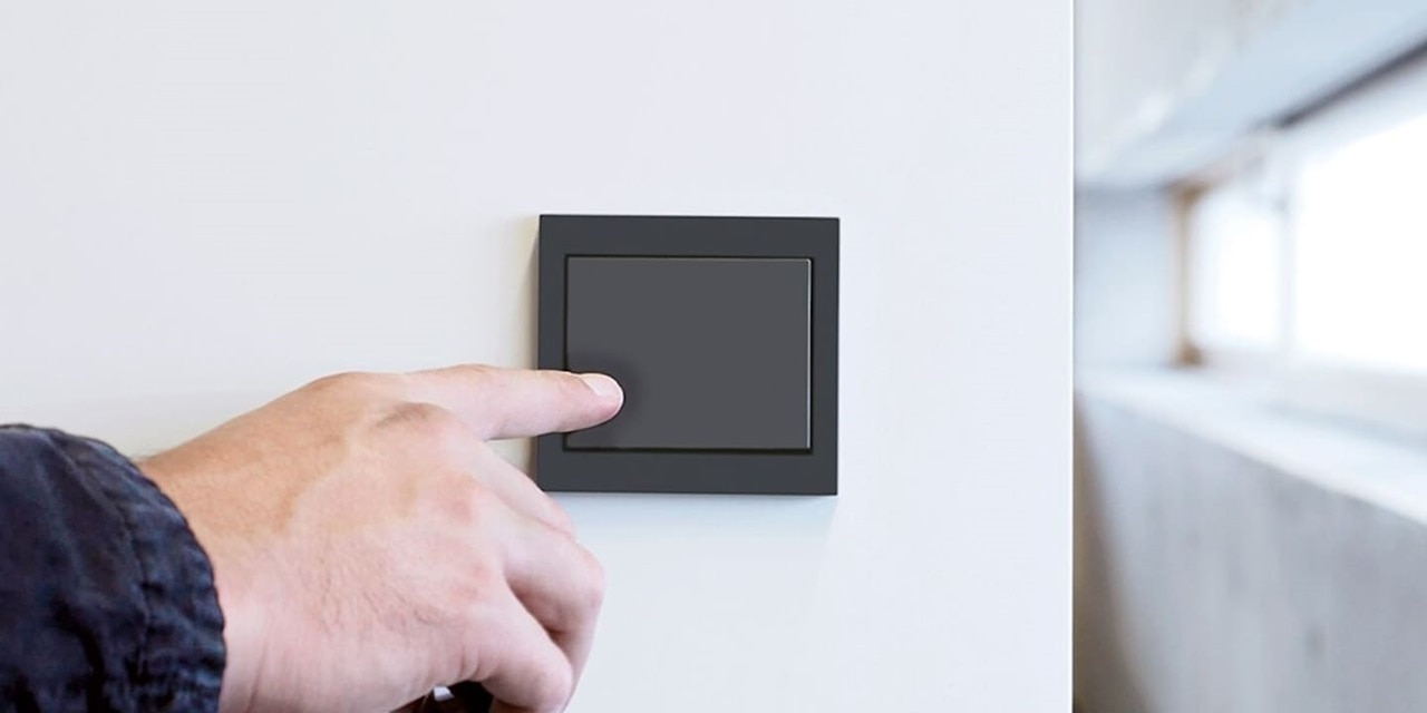 Una mano maschile preme l'interruttore Berker K.1 in primo piano, installato su parete bianca