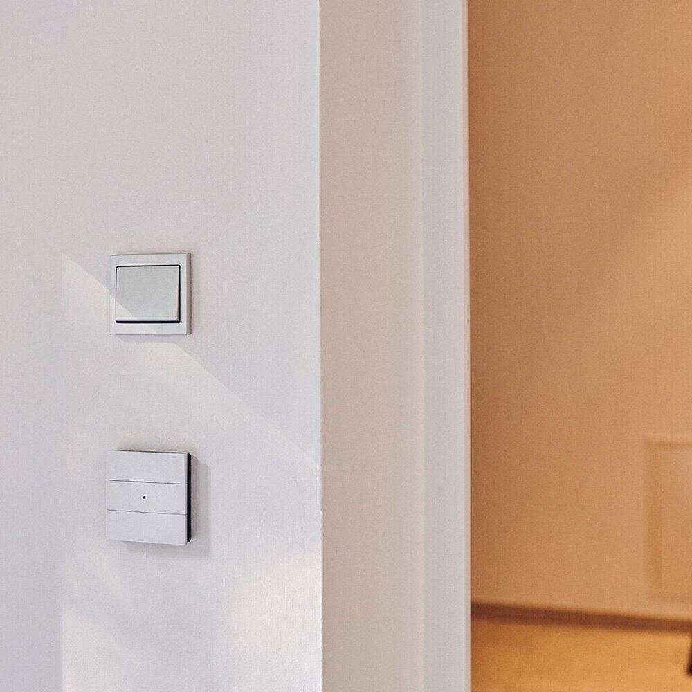 Vista frontale di un interruttore della serie civile di design Berker K.5 in plastica color bianco installata a parete, sopra a una presa KNX