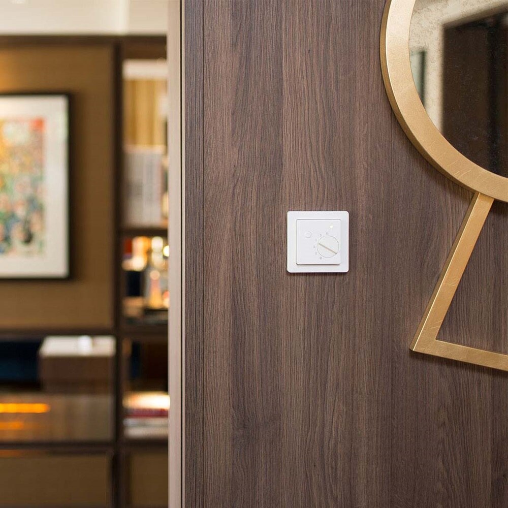 Vista frontale di un regolatore di temperatura di colore bianco della serie Berker Q.1 montato su una parete di legno scuro in una stanza di hotel