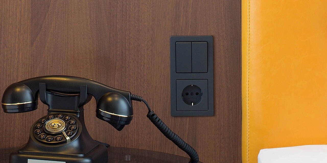 Esempio di installazione dell'interruttore della luce e della presa Berker Q.1 in nero su una parete in legno di una camera di hotel. In primo piano telefono antico.
