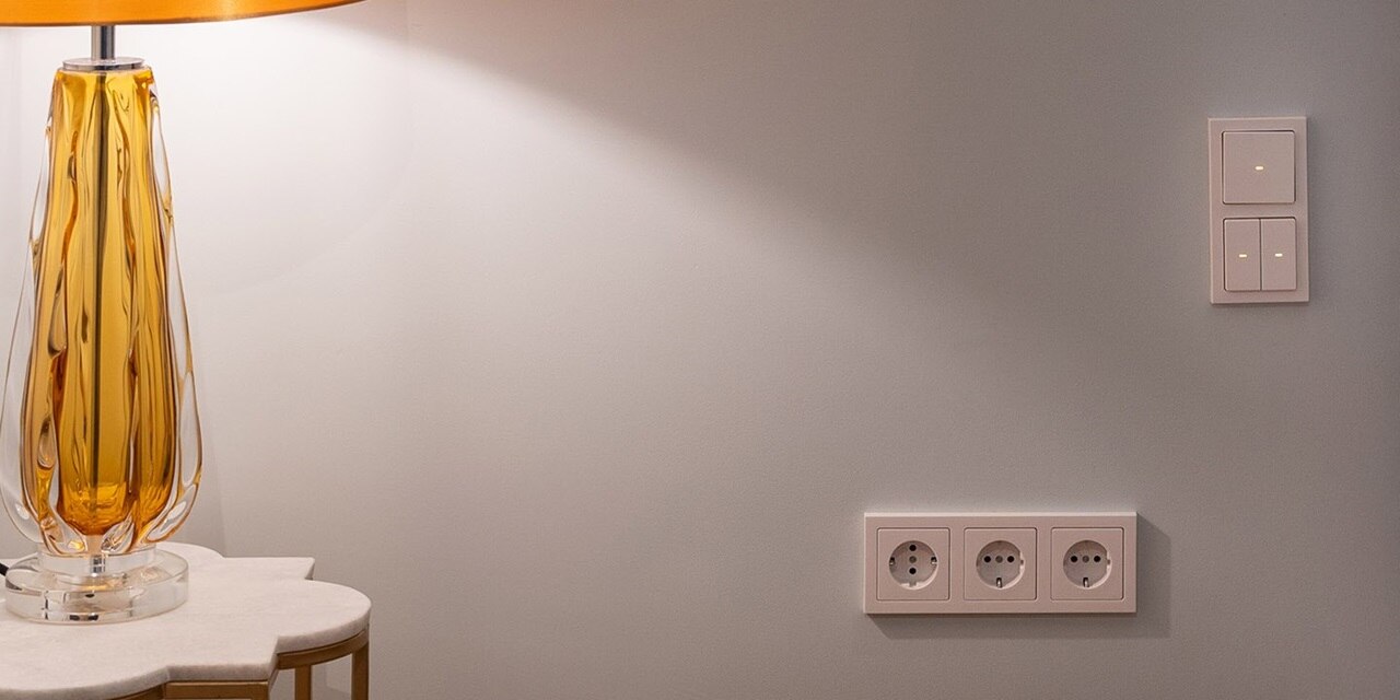 Vista di una camera d'albergo con letto e prese Berker Q.3 e interruttori della luce bianchi per il controllo dell'illuminazione.