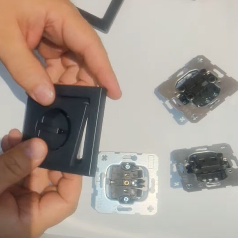 Mani che tengono una cornice e una presa Berker Q.7 mentre sul tavolo sono posizionati tre inserti