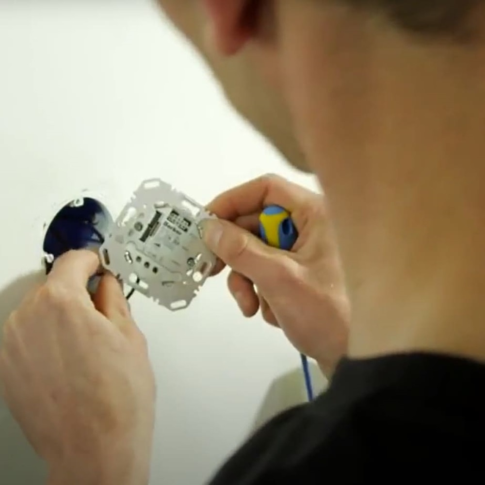 Installatore di spalle mentre installa telaio interruttore Berker nella scatola nella parete di fronte