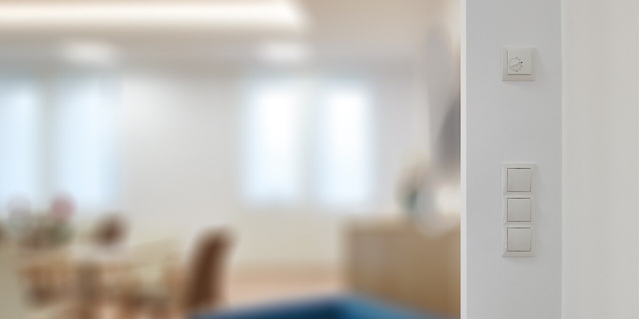 Esempio di installazione del regolatore di temperatura Berker S.1, interruttore della luce con cornice a 3 moduli in bianco su una parete bianca