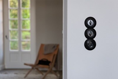 Esempio applicativo verticale di cornice a tre moduli di interruttori Berker Serie 1930 su parete, in ambito residenziale