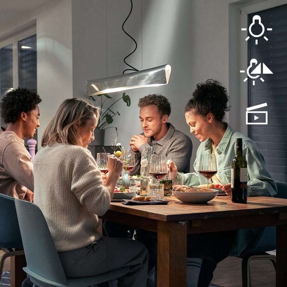 Quattro persone che mangiano a un tavolo con una lampada moderna in alto, a destra tre pittogrammi per l'illuminazione, la luminosità della luce e gli scenari di illuminazione