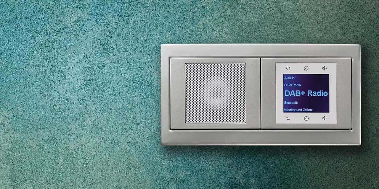 Esempio di installazione della radio Berker da incasso con display, elementi di comando e altoparlante con cornice in alluminio della serie di interruttori e prese K.5 su una parete con intonaco decorativo/effetto gesso blu