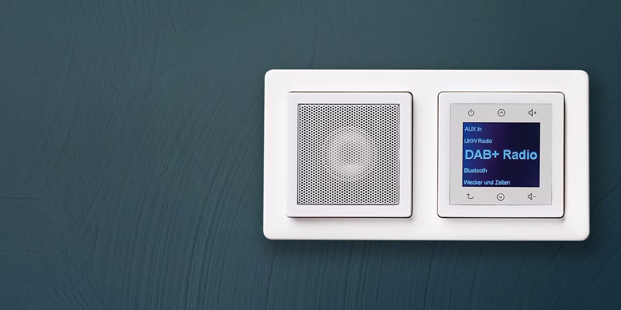 Esempio di installazione di una radio Berker da incasso con display, comandi e altoparlante con cornice bianca della serie di interruttori e prese Q.1 su una parete con intonaco testurizzato blu