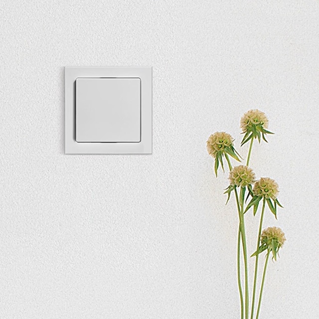 Vista frontale del sensore KNX CO2 installato, montaggio a filo in una parete bianca con fiori visibili sulla destra