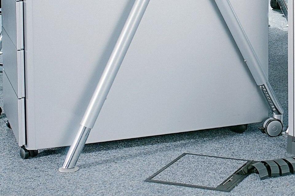 Close-up of a metal cabinet leg with adjustable support and a floor cable cover