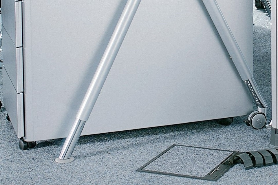 Close-up of a metal cabinet leg with adjustable support and a floor cable cover