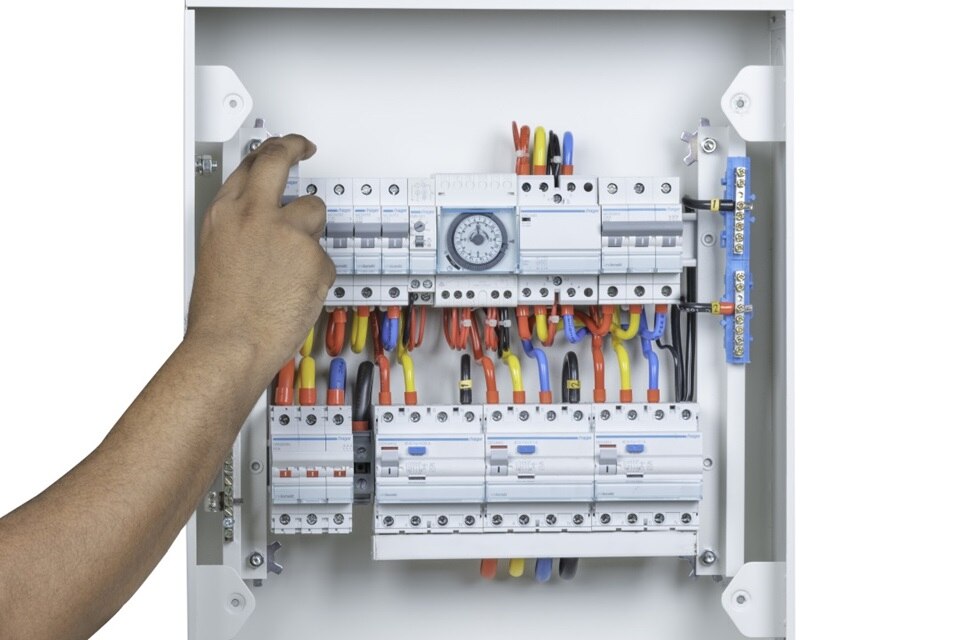 Person installing a timer in an electrical panel with circuit breakers and organized wiring