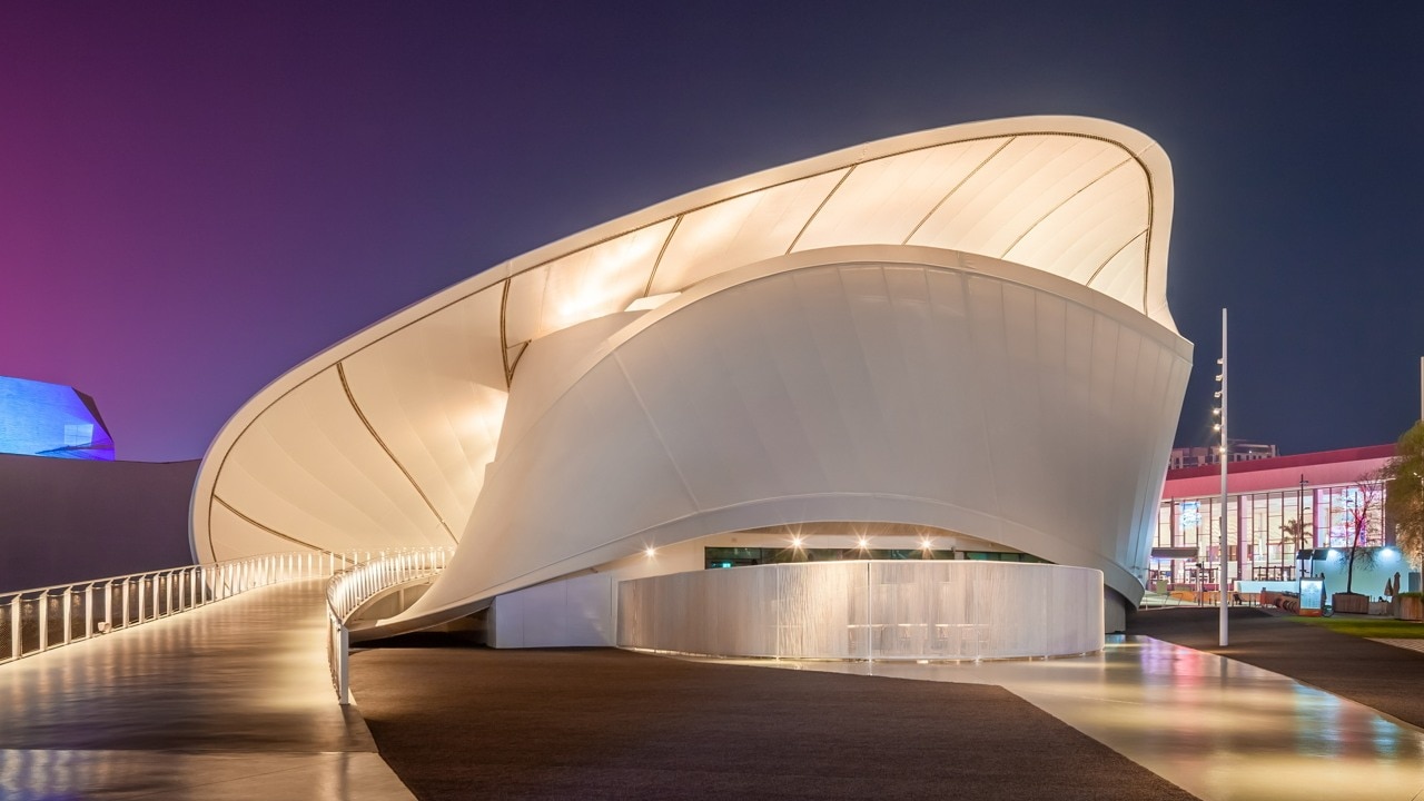 Modern architecture of a white building with a curved design and illuminated walkway at dusk