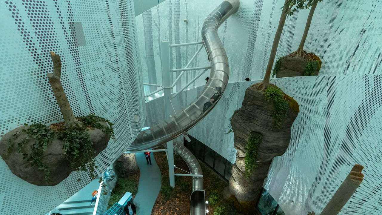 Indoor slide in a modern atrium surrounded by greenery and perforated metal sheets