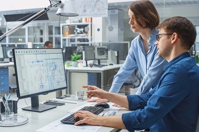 Two professionals analyzing electrical schematics on a computer monitor in a modern office