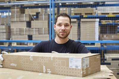 Employee in a warehouse handling a cardboard box with storage racks in the background