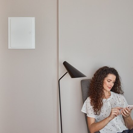 vrouw zit op een stoel met tegen de muur links een gesloten elektriciteitskast (volta) van Hager