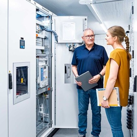 Installateur met tablet in de hand met vrouw met documenten kijken naar een elektrische verdeelkast van Hager