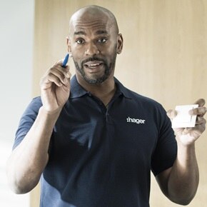 Persoon in Hager-kledij houdt een pen en een witte schakelaar vast in een neutrale, professionele omgeving.