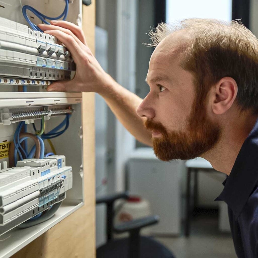 Persoon inspecteert een elektrisch paneel met verschillende stroomonderbrekers en bedrading in een technische omgeving.