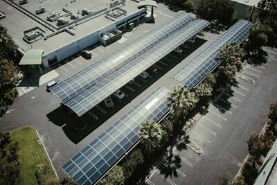 Luchtbeeld van parkeerplaatsen met carports voorzien van zonnepanelen, die zowel bescherming voor voertuigen als zonne-energieopwekking bieden.