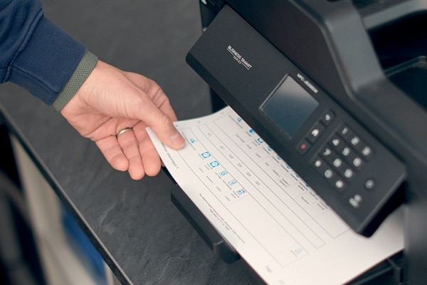 Persoon haalt geprint document uit een printer; het papier bevat labels voor een elektrische verdeelkast