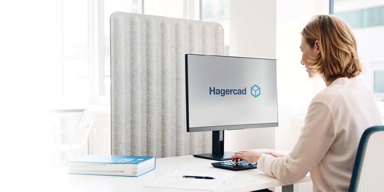 Persoon aan bureau werkt met Hagercad-software op het scherm, omringd door papieren, pen en boek in een moderne kantooromgeving.