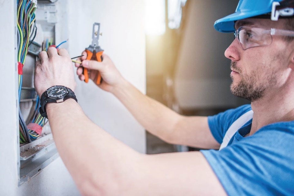 Electrician wearing a hard hat and safety glasses working on an electrical panel with wires