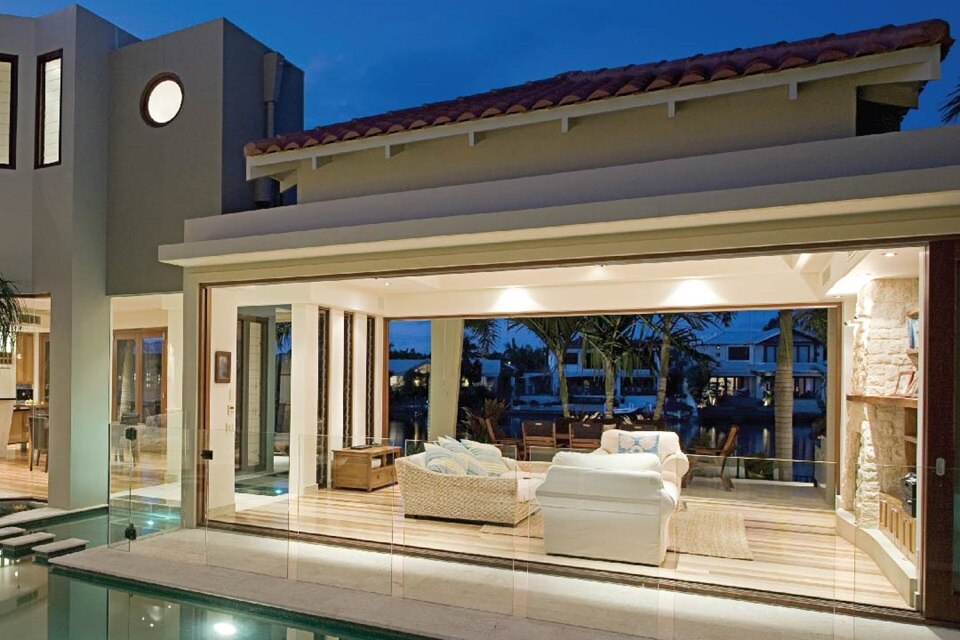 Modern house exterior at dusk with illuminated interior and outdoor lighting, featuring a pool and waterfront view
