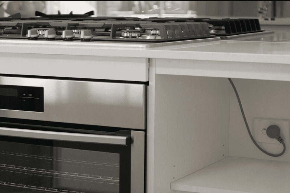 Modern kitchen interior showcasing a gas stove, built-in oven, and an electrical outlet with a plugged-in device