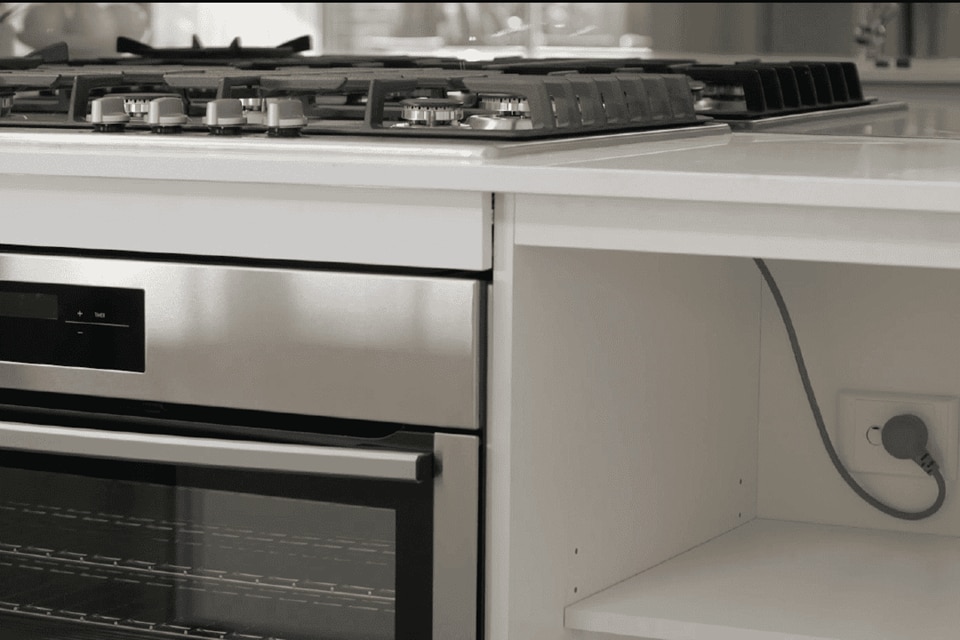 Modern kitchen interior showcasing a gas stove, built-in oven, and an electrical outlet with a plugged-in device