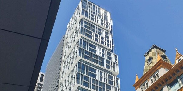 Modern skyscraper next to a historic building against a clear blue sky