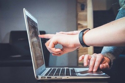 Osoba wskazująca na ekran laptopa, z naciskiem na współpracę i technologię