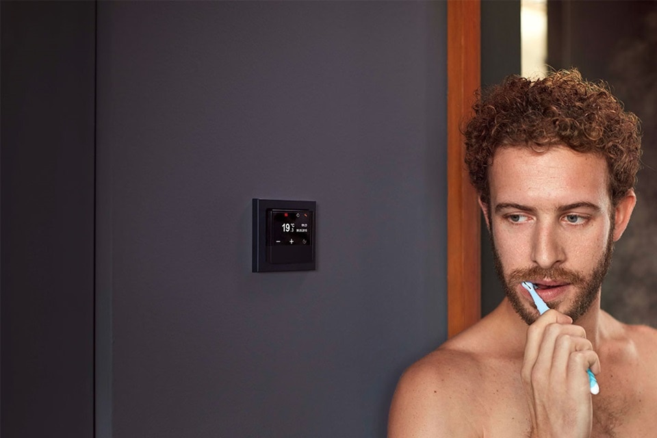 Osoba goli się przed lustrem z inteligentnym termostatem na ścianie wyświetlającym temperaturę