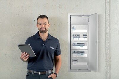 Pracownik firmy Hager z tabletem obok otwartej rozdzielnicy elektrycznej z wyświetlaczami obwodów i jednostkami dystrybucji