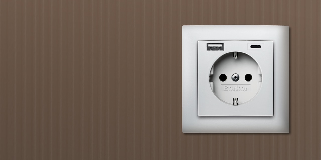 Frontalansicht Berker S.1 Steckdose mit 2-fach USB-Ladedose (1x USB-A, 1x USB-C) mit Rahmen in Weiß auf braunem Hintergrund
