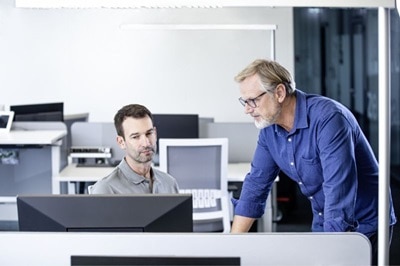 Dwóch projektantów instalacji elektrycznych siedzących przy komputerze i korzystających z narzędzia Hager Protection Coordinator