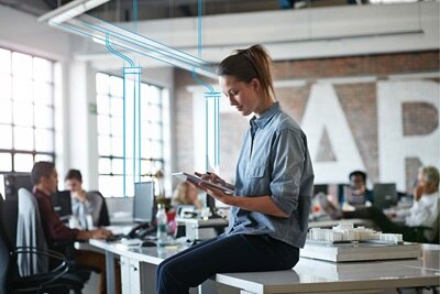 Osoba korzystająca z tabletu w nowoczesnym biurze z naturalnym oświetleniem i pracującymi w tle kolegami z pracy