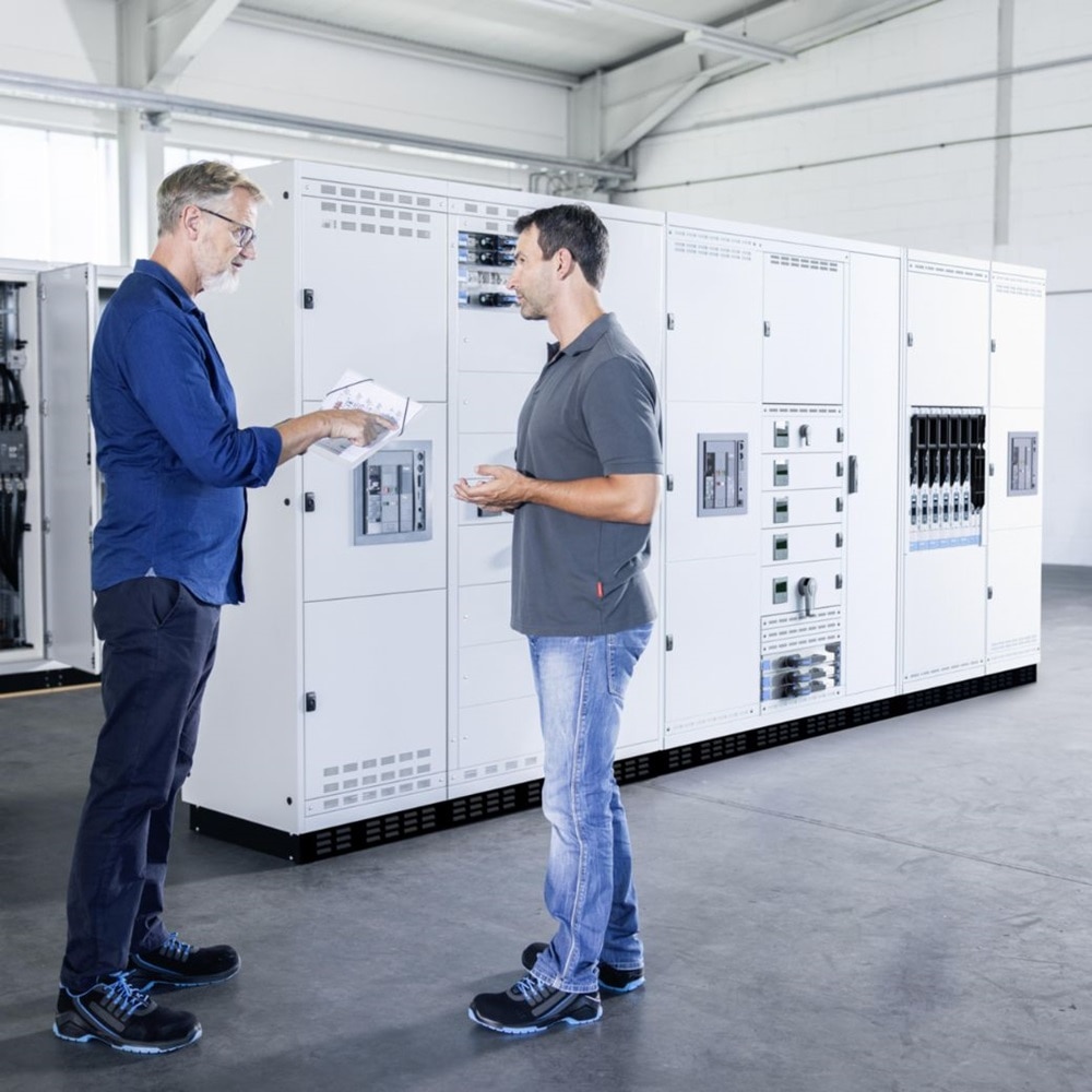 Dwoje mezczyzn stojacych przy systemie dystrybucji energii unimes H firmy Hager