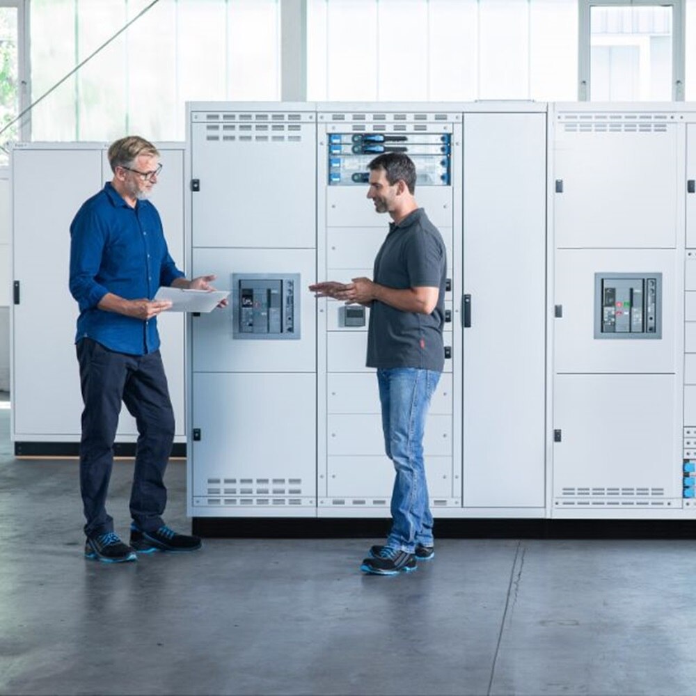 Dwóch mężczyzn stojących przed rozdzielnicą unimes H firmy Hager