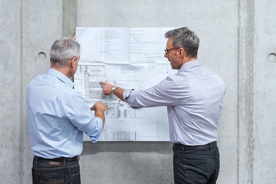Dwóch profesjonalistów dyskutujących nad planami budowlanymi na placu budowy